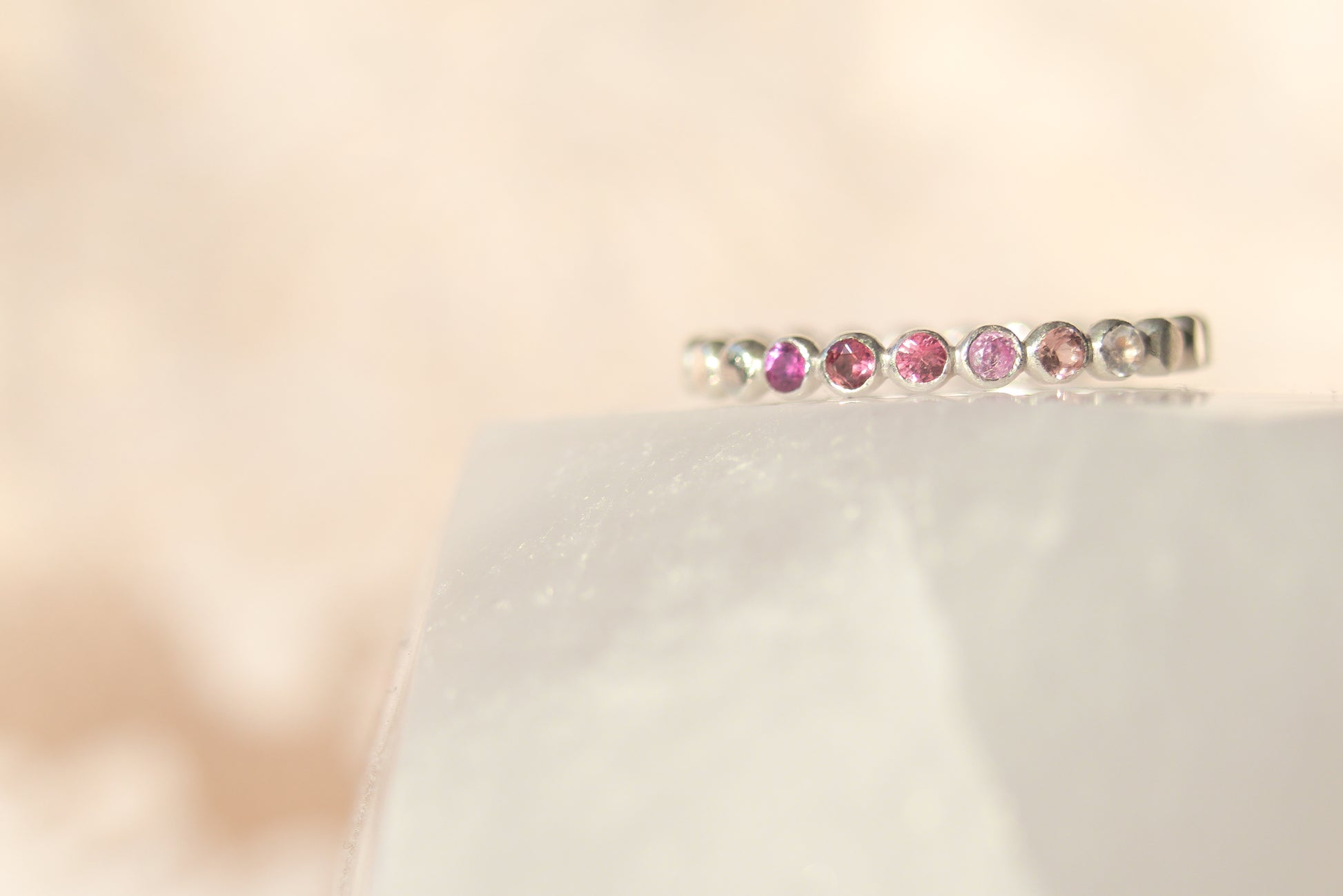 Silver ring with pink gemstones on a white cushion against a beige background